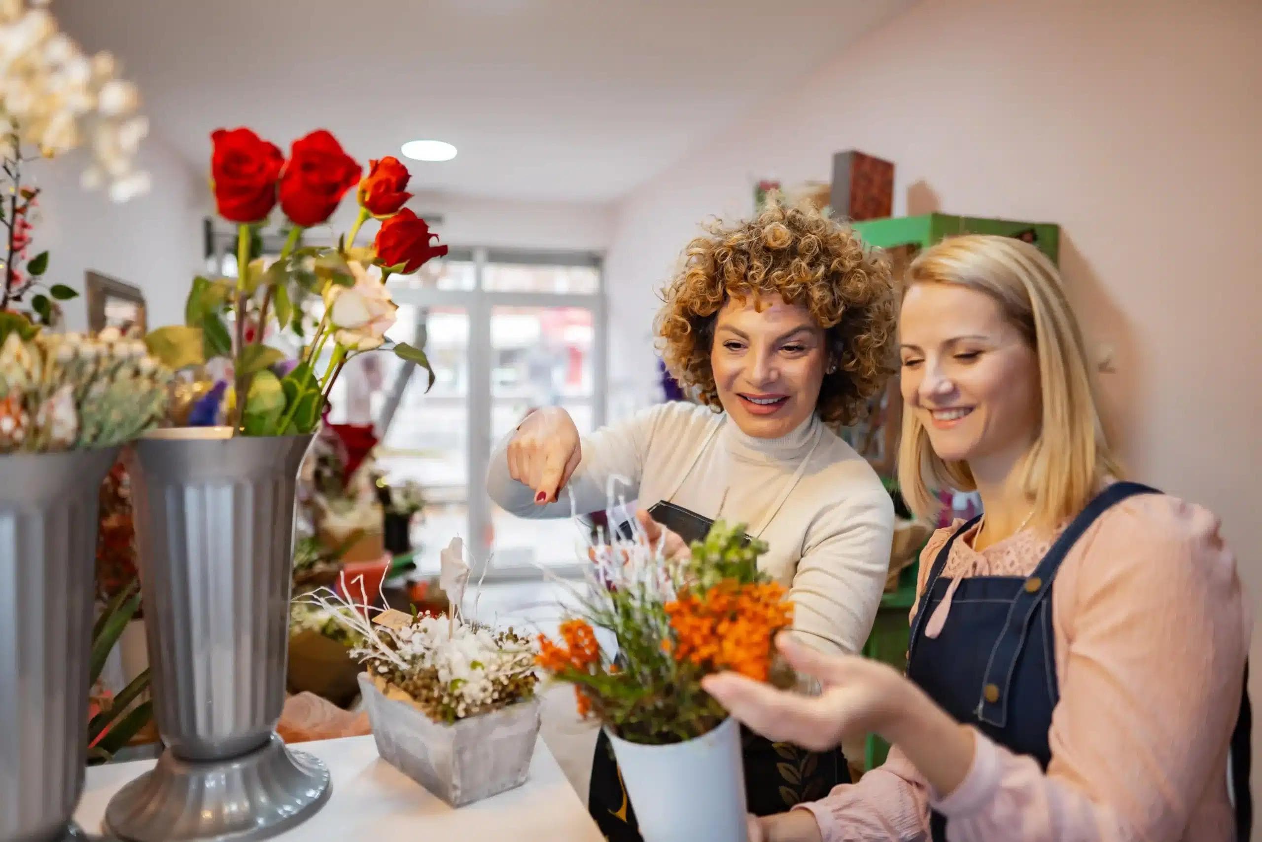 Dwie radosne kobiety w kwiaciarni komponują bukiet kwiatów.