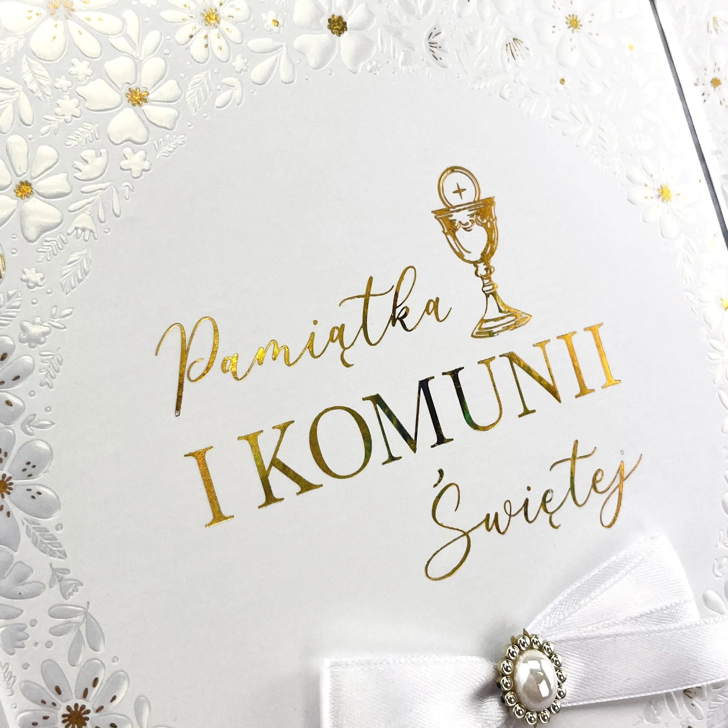 Zdjęcie albumu a4 na Komunię pod kątem, pokazuje wszystkie szczegóły zdobień, wzór w tłoczone kwiatki z kokardką zbliżenie