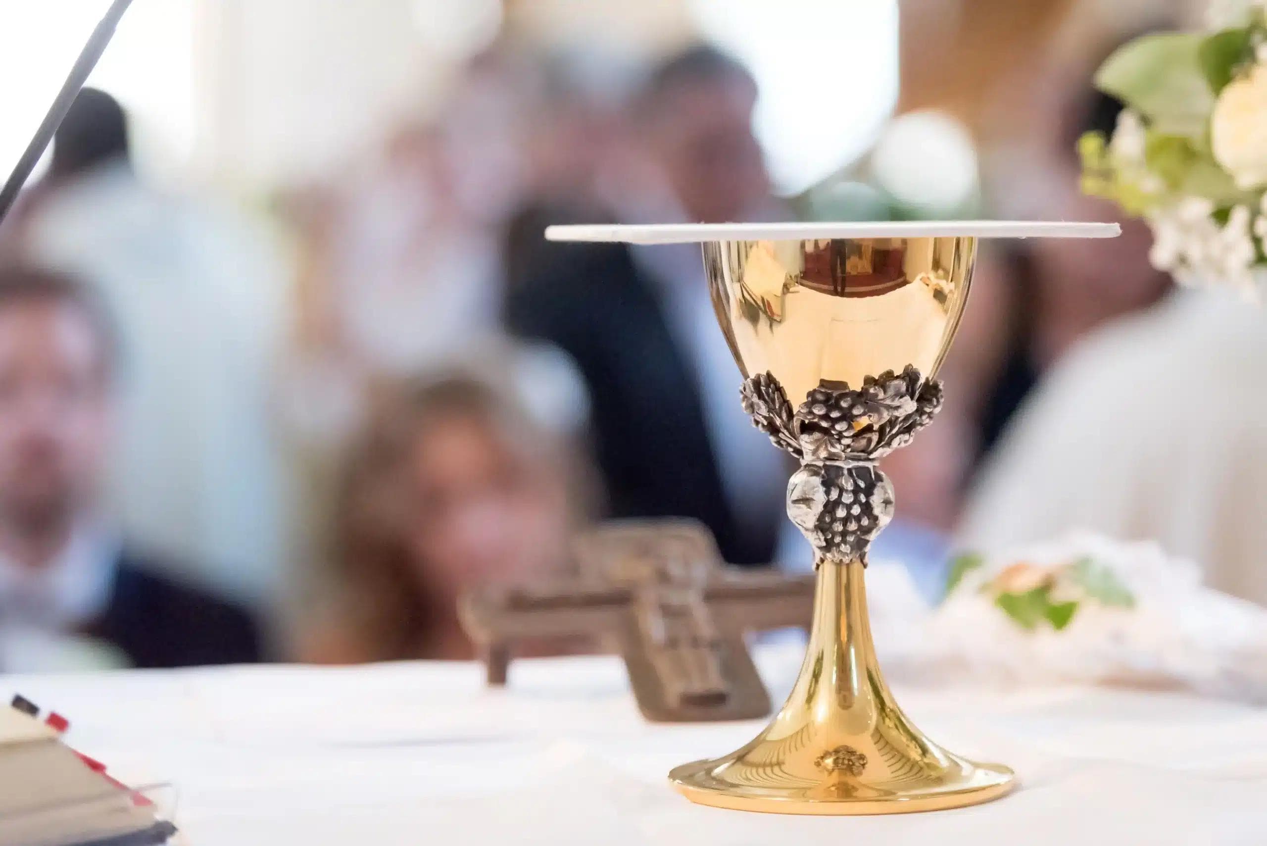 Komunia Święta – kielich i krzyż na ołtarzu w kościele, w tle wierni.