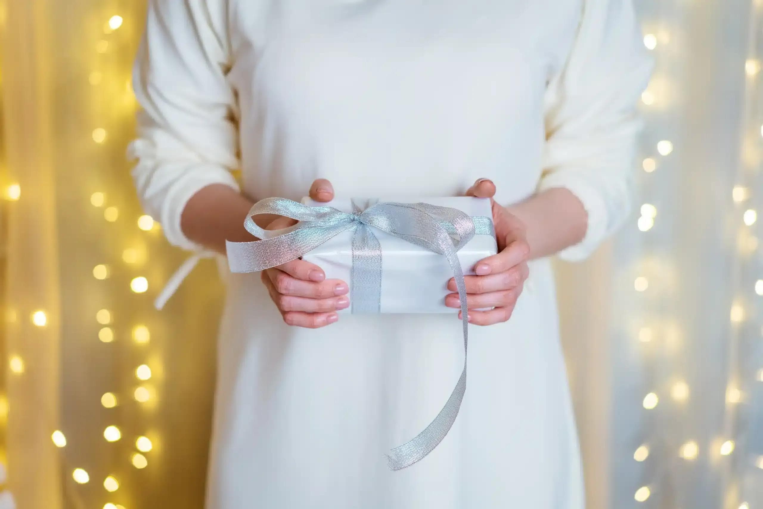 Osoba w białym ubraniu trzymająca prezent komunijny.
