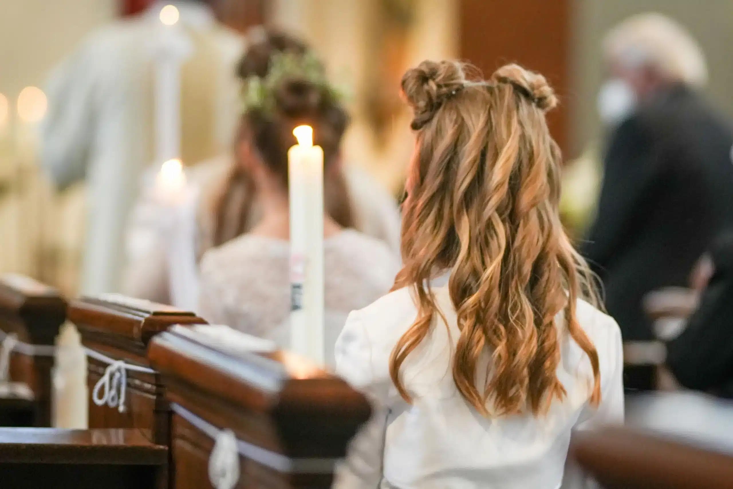 Dziewczynka stojąca tyłem w kościele przystępuje do Komunii, ma na sobie białą sukienkę.